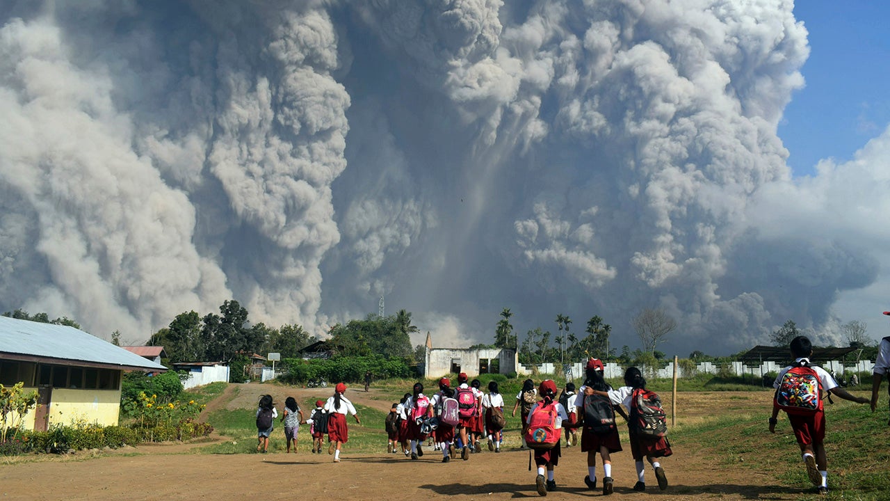 School children walk as Mount Sinabung erupts in Karo, North Sumatra, Indonesia, Monday, Feb. 19, 2018. Rumbling Mount Sinabung on the Indonesian island of Sumatra has shot billowing columns of ash more than 16,400 feet into the atmosphere and hot clouds down its slopes.  The volcano, one of three currently erupting in Indonesia, was dormant for four centuries before exploding in 2010.(AP Photo/Sarianto)               