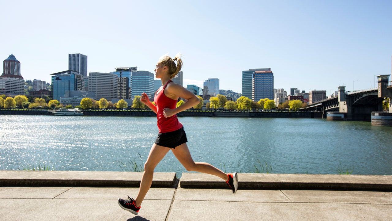 A young woman running along the Portland waterfront trail with the city in the background.