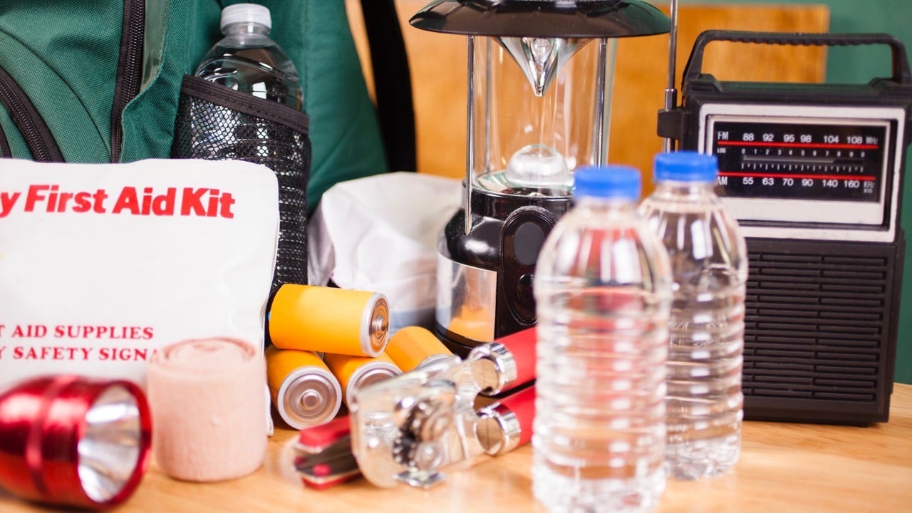 Emergency preparedness supplies. A large pile of supplies to be used in case of a natural disaster (hurricane, flood, earthquake, etc.) including: flashlight, backpack, batteries, water bottles, first aid kit, lantern, radio, can opener, mask.  No people.