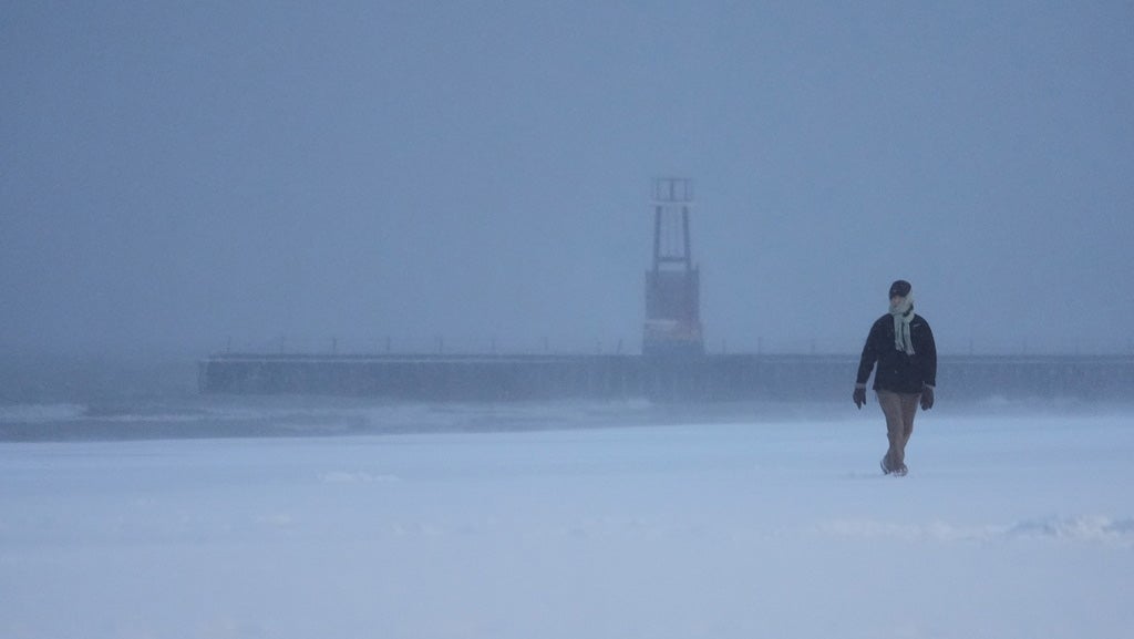 A bundled up person walks on a beach along Lake Michigan, Saturday, Nov. 29, 2025, in Chicago. (AP Photo/Kiichiro Sato)