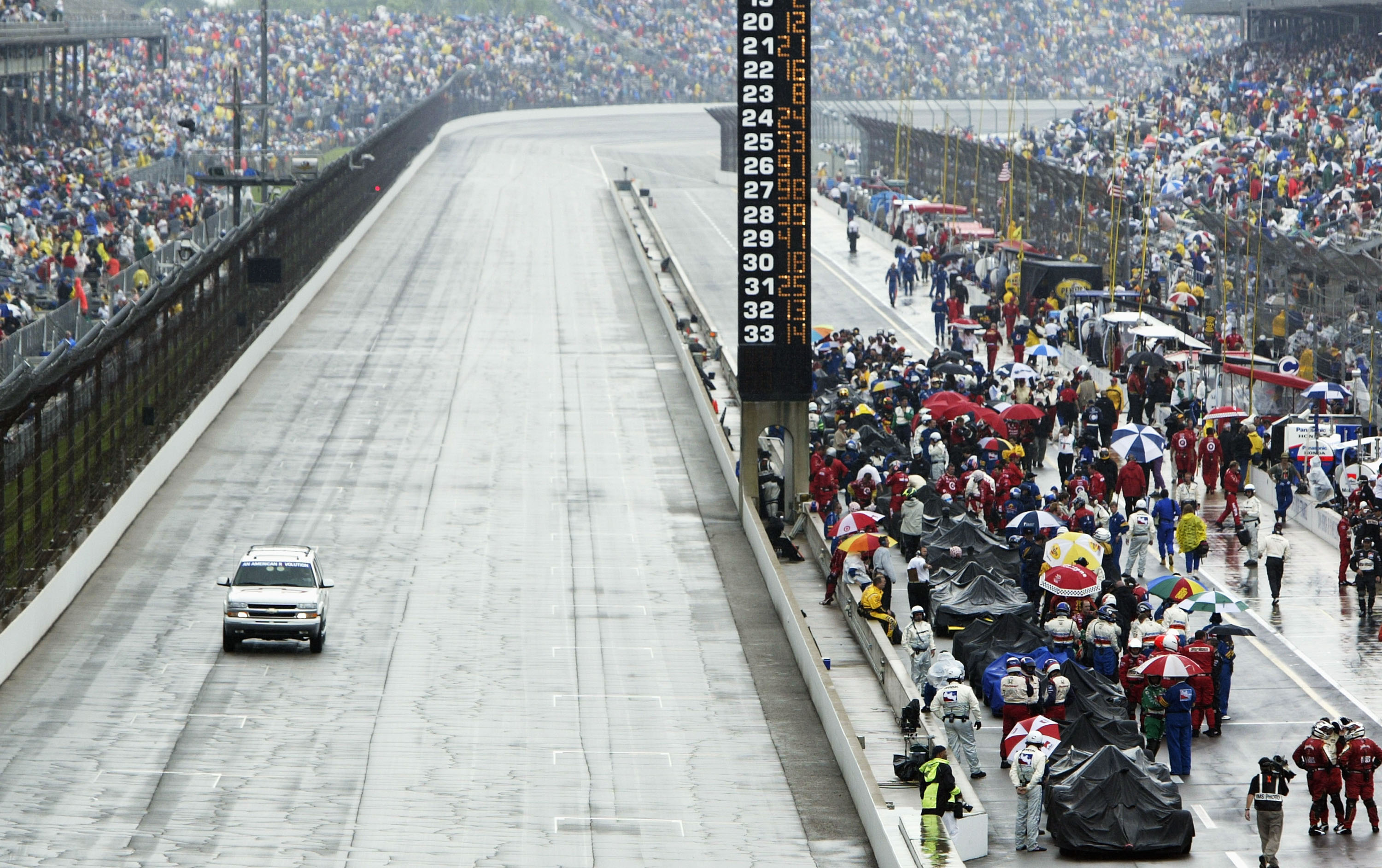 Indy race cars sit under covers during a rain storm.