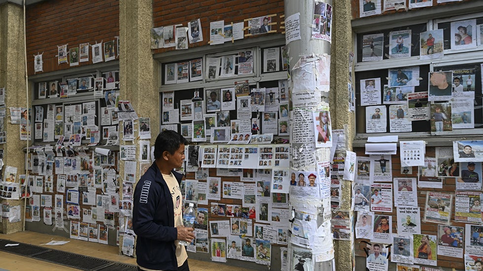 A man looks at a wall covered in missing people flyers.
