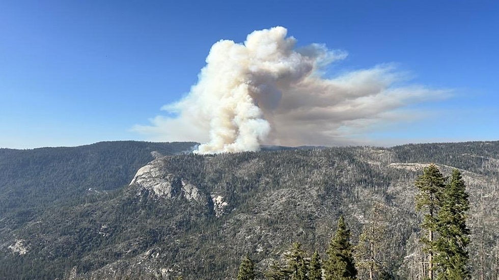 A tall cloud of smoke rises over a stretch of mountains