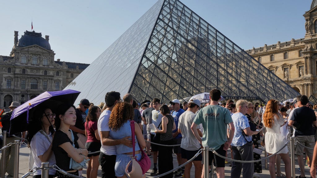 Tourists line up under an umbrella for shade outside the Louvre Museum as temperatures are expected to reach record highs in Paris, Wednesday, June 24, 2026. 