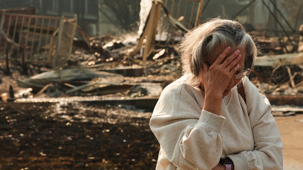 Distressed woman covers face with hand while standing amid rubble and debris of a burned-out structure