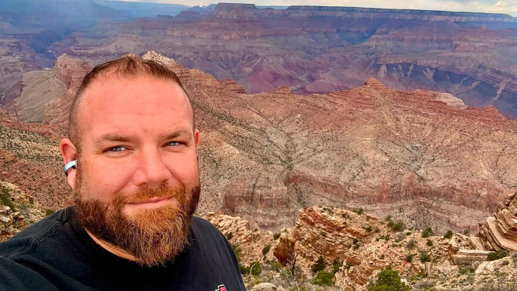Bearded man smiling for a selfie with the vast rocky canyon landscape of the Grand Canyon in the background.