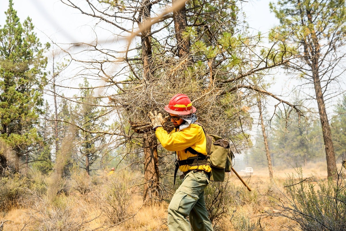 A firefighter clears vegetation as the Akawa Butte fire approaches on Friday, July 24, 2026, near Sisters, Oregon.