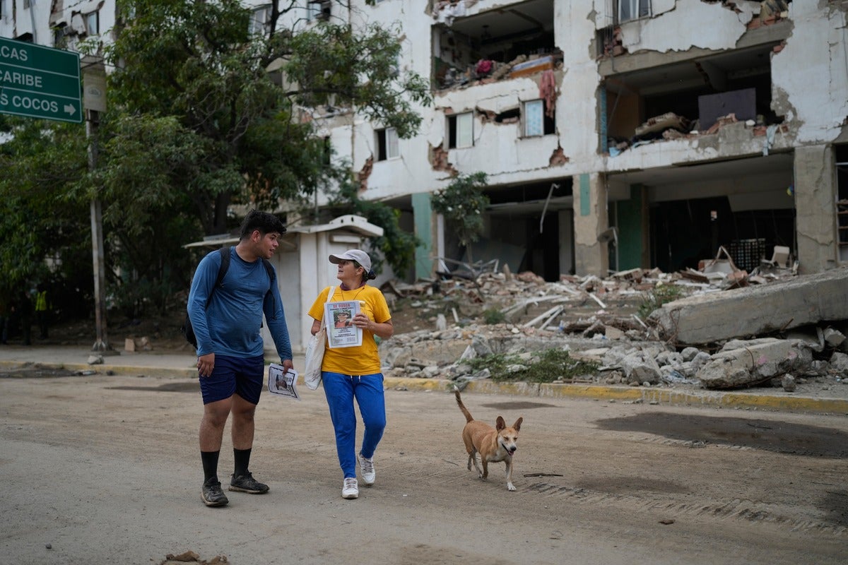 people and dog stand in front of destroyed building