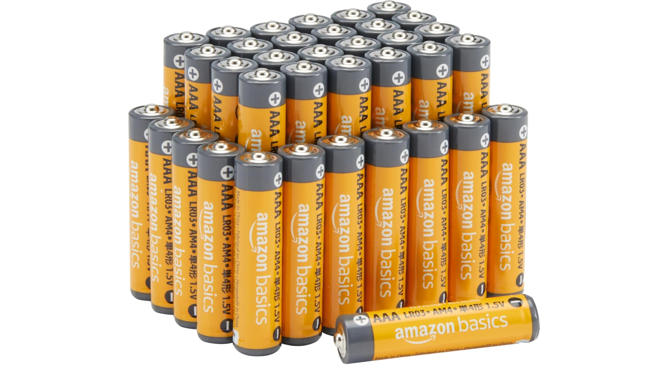 Large collection of orange and gray Amazon Basics AAA alkaline batteries arranged in multiple rows with one battery lying horizontally in front