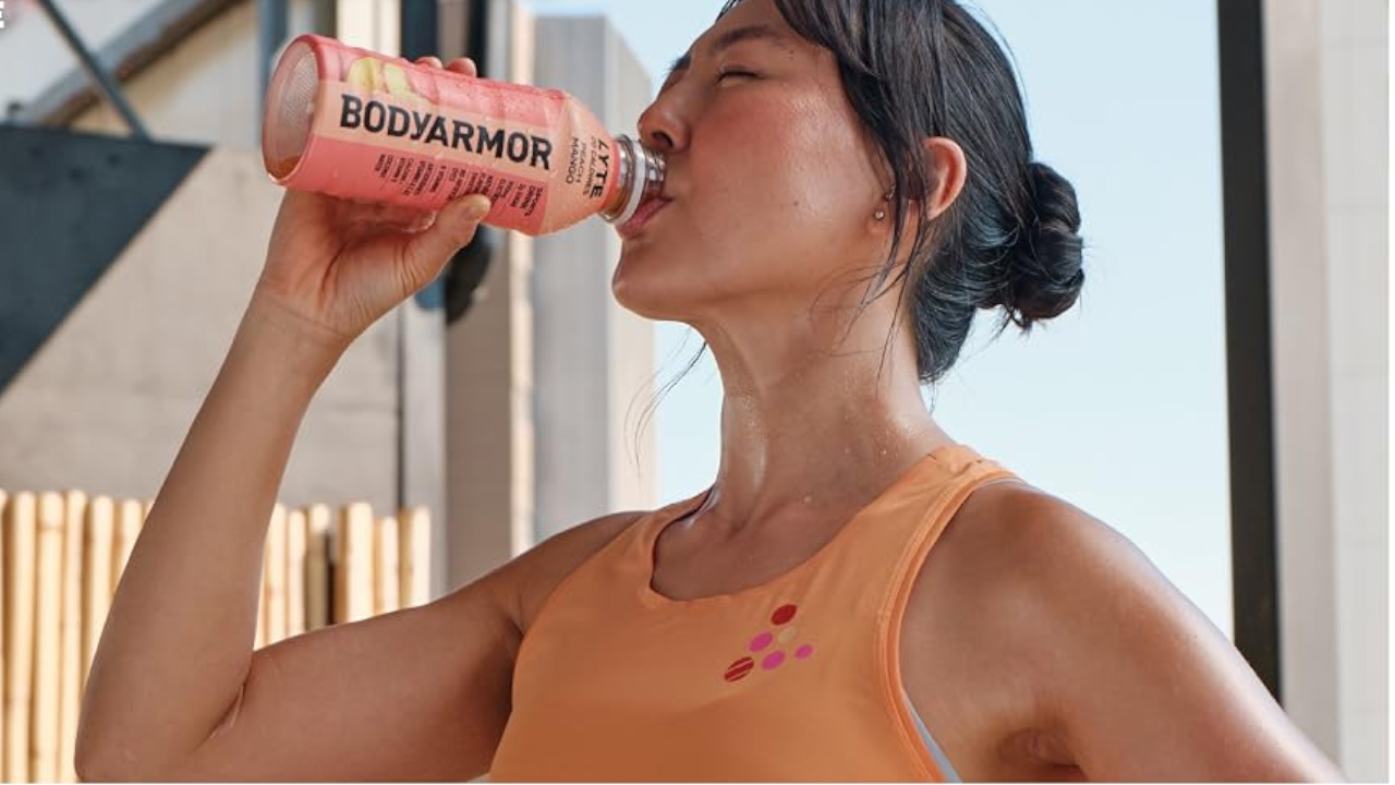 Woman in an orange athletic top drinking from a pink BODYARMOR bottle