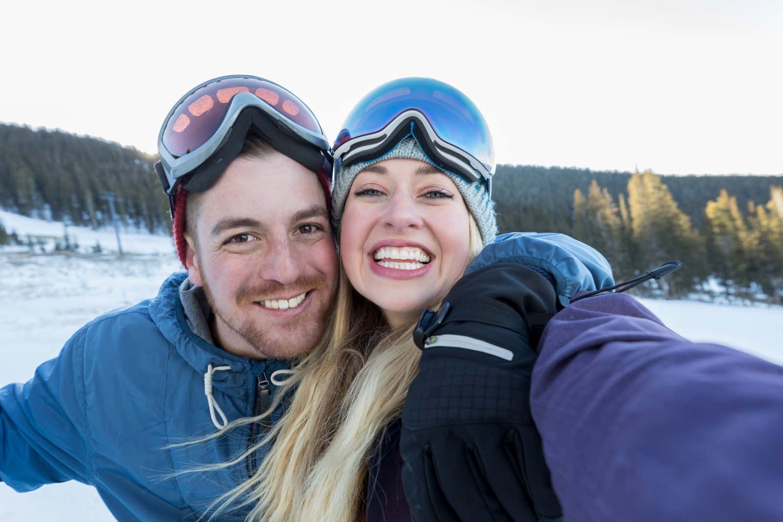 A man and woman smiling and taking a selfie on a snowy mountain in Colorado, with ski or snowboard gear visible.