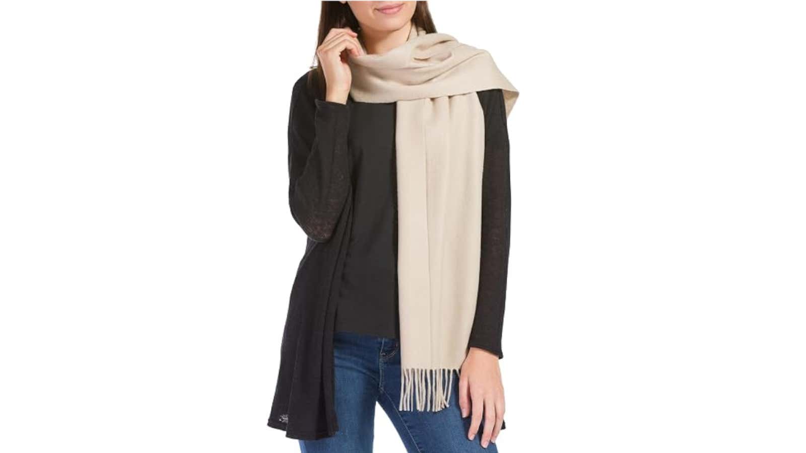 Woman wearing a black cardigan over black top with a beige fringed scarf draped around her neck