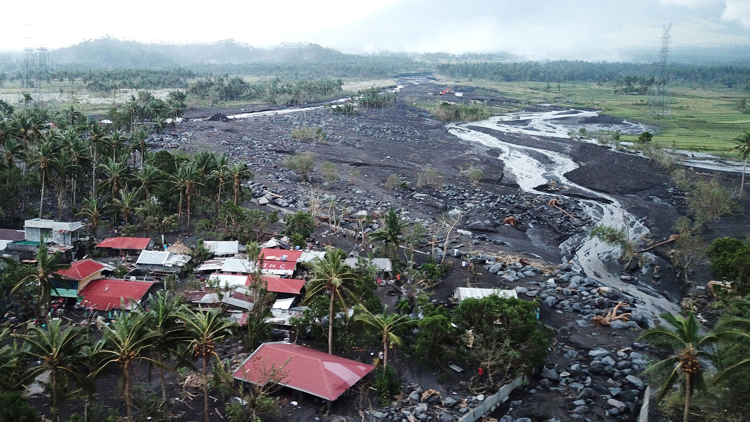 Village with red-roofed houses surrounded by black volcanic lava flow with white mineral deposits cutting through tropical landscape