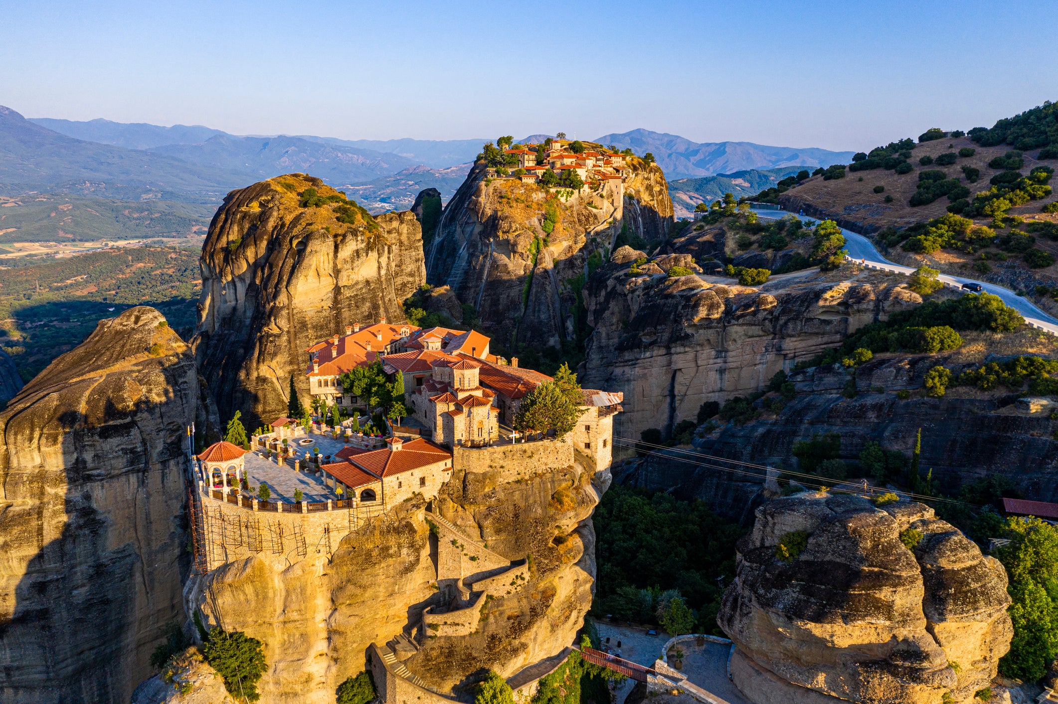 Aerial view of Meteora monasteries perched atop towering rock pillars in Greece, surrounded by mountainous landscape.