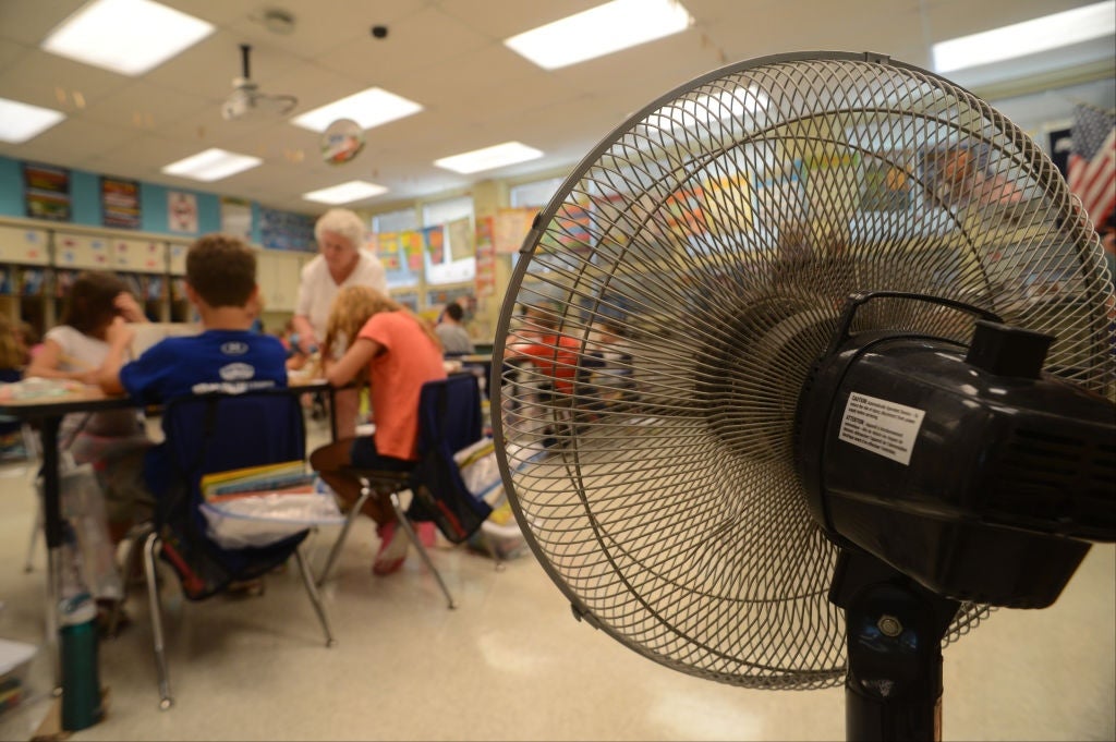 Students try to keep cool with the help of a fan, while inside a hot classroom. 