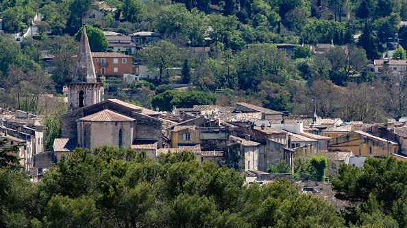 Stone church with tall steeple among village rooftops and trees on a hillside.