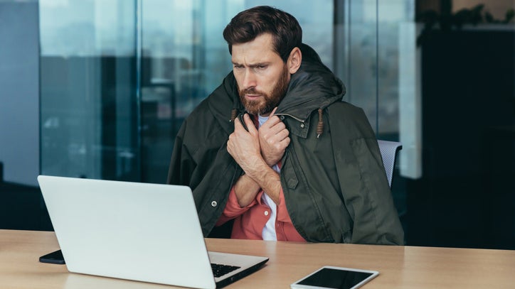 A man wraps himself in a blanket as he tries to stay warm in a cold office.