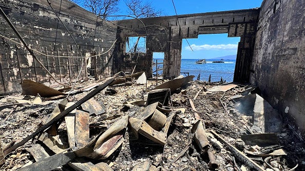 Charred remains of a fire-destroyed building with debris scattered on the floor, overlooking the ocean through a burned-out window.