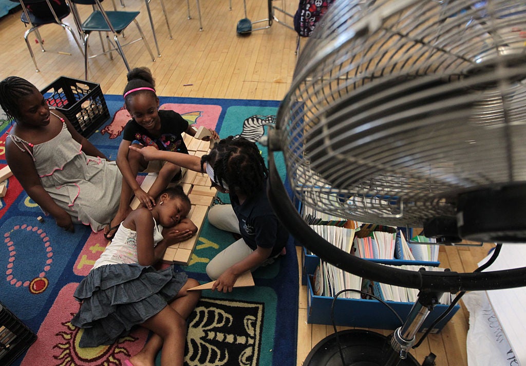 Students trying to cool off with the help of a fan inside a hot classroom. 