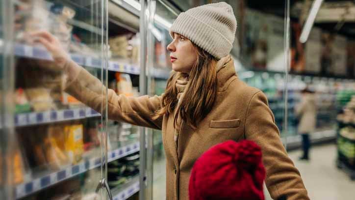 Woman in beanie and coat selecting items from a supermarket aisle.