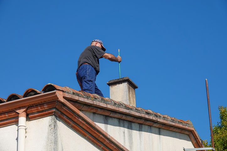 A person works on a chimney atop a house.