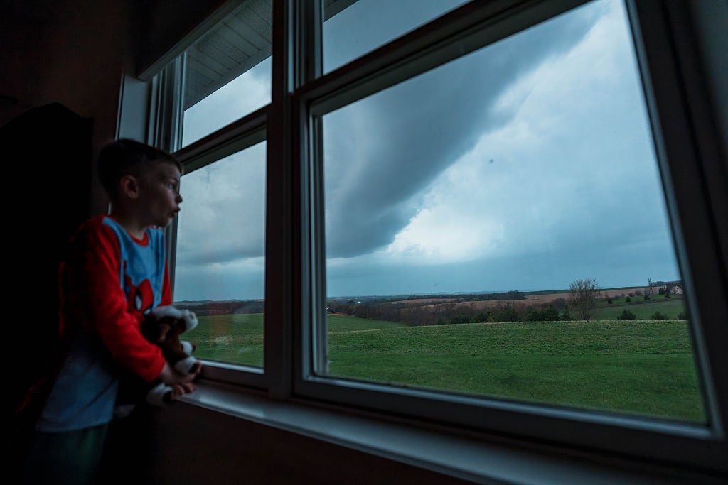 A young boy watches dark storm clouds from a bedroom window as severe weather affects the Midwest on April 14, 2026. 