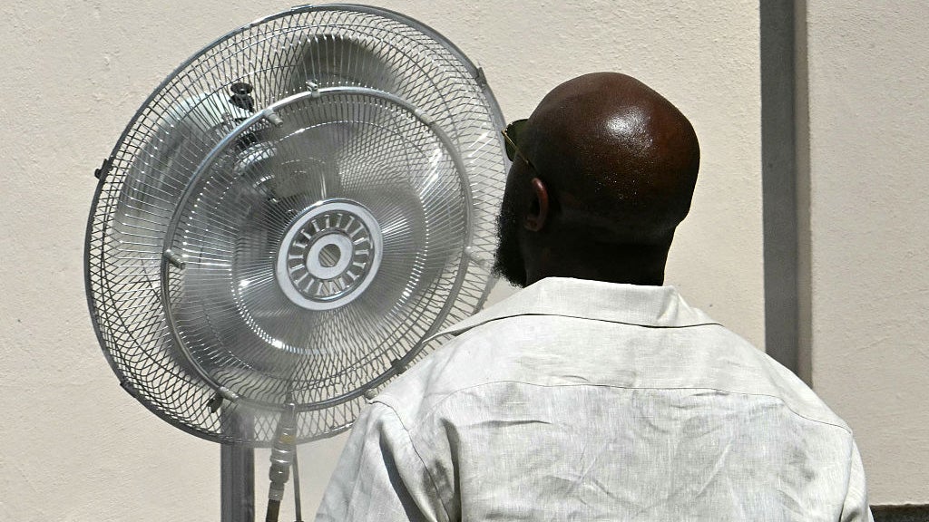 A guest stands in front of a fan to cool down before the Thom Browne collection show at Milan's Fashion Week Menswear Spring/Summer 2027, in Milan on June 22, 2026. 