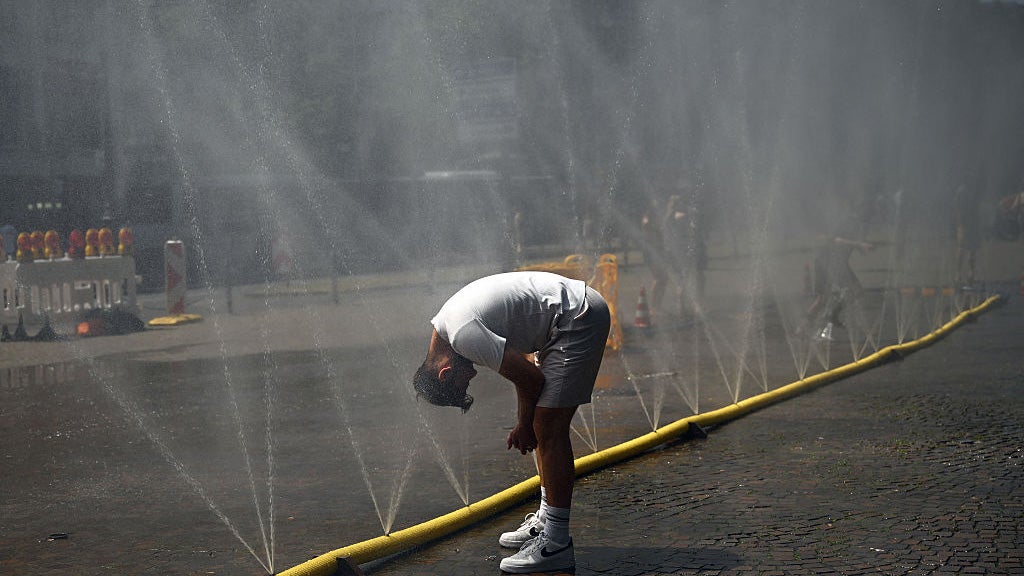 A man cools his head at water a hose spraying water.