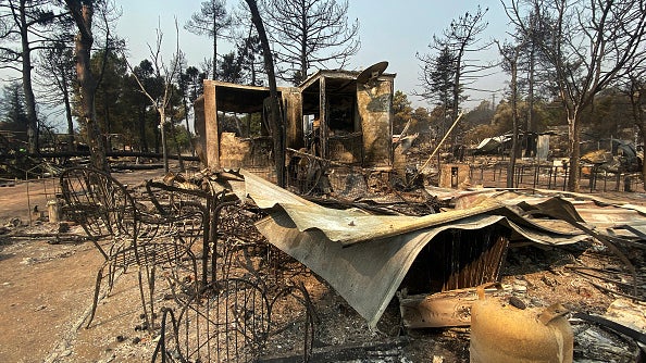 Burned remains of a house amid charred trees and twisted metal after a wildfire