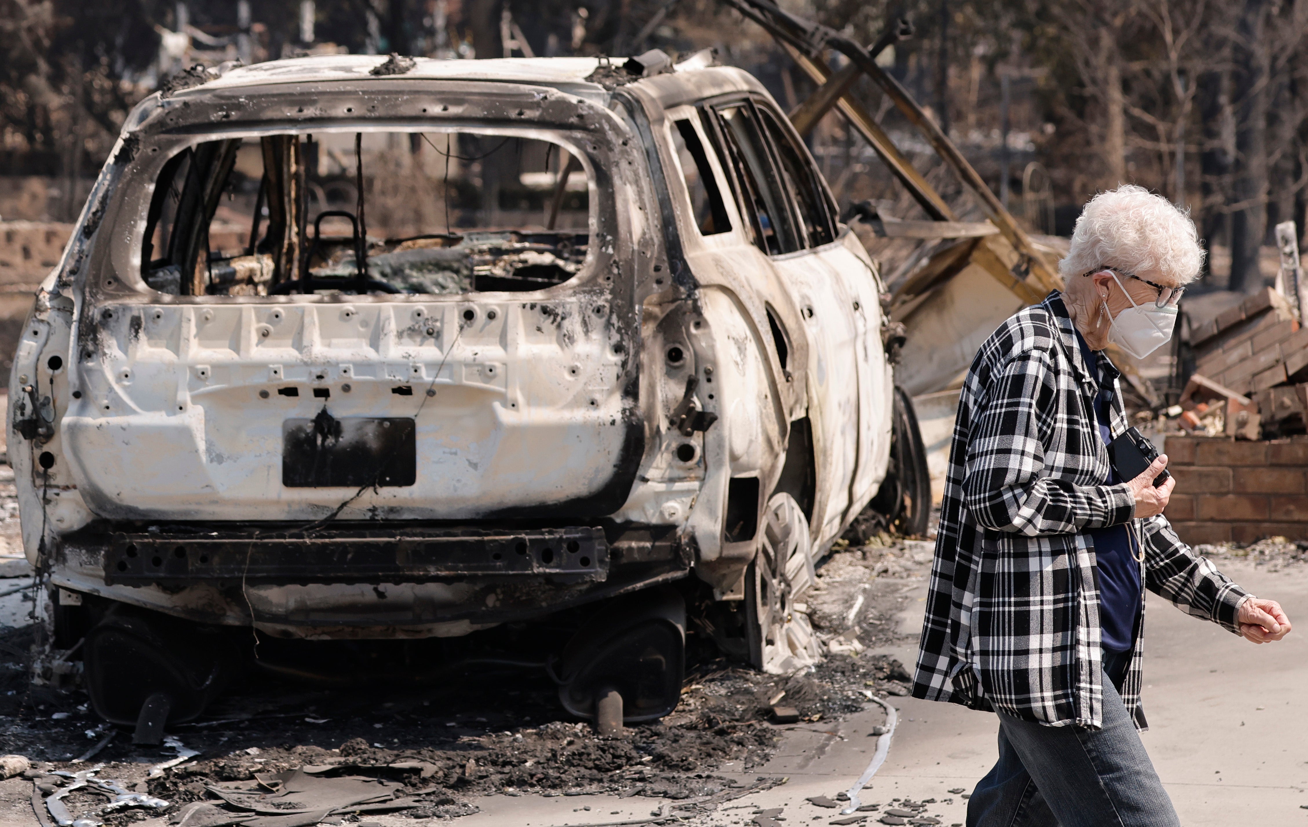 A person wearing a face mask amid poor air quality walks past a home destroyed in the Old Trails Fire on August 5, 2026 in Spokane, Washington. 
