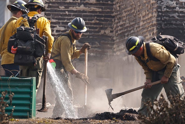 Moses Lake Fire Department firefighters work to extinguish hotspots at a home destroyed in the Old Trails Fire on August 5, 2026 in Spokane, Washington.