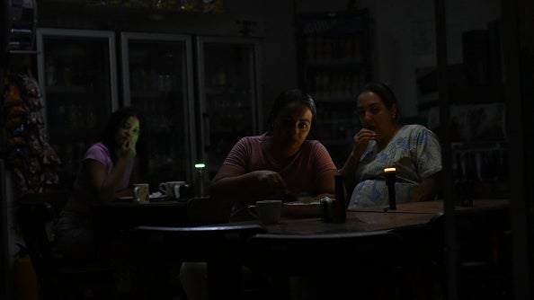 Three women sit at tables in a dimly lit shop illuminated by small green and orange indicator lights.