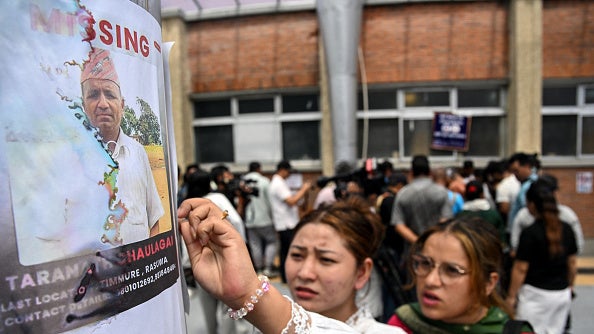 Woman posts a "Missing" flyer with a man's photo on a pole as a crowd gathers behind her.