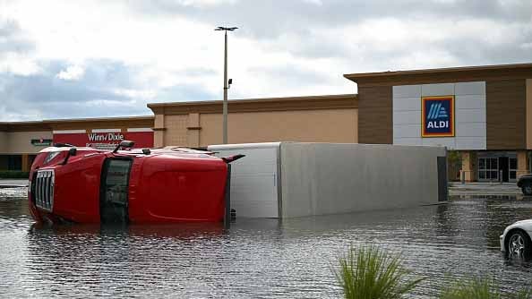 Overturned red truck and trailer in floodwater outside Winn-Dixie and Aldi stores