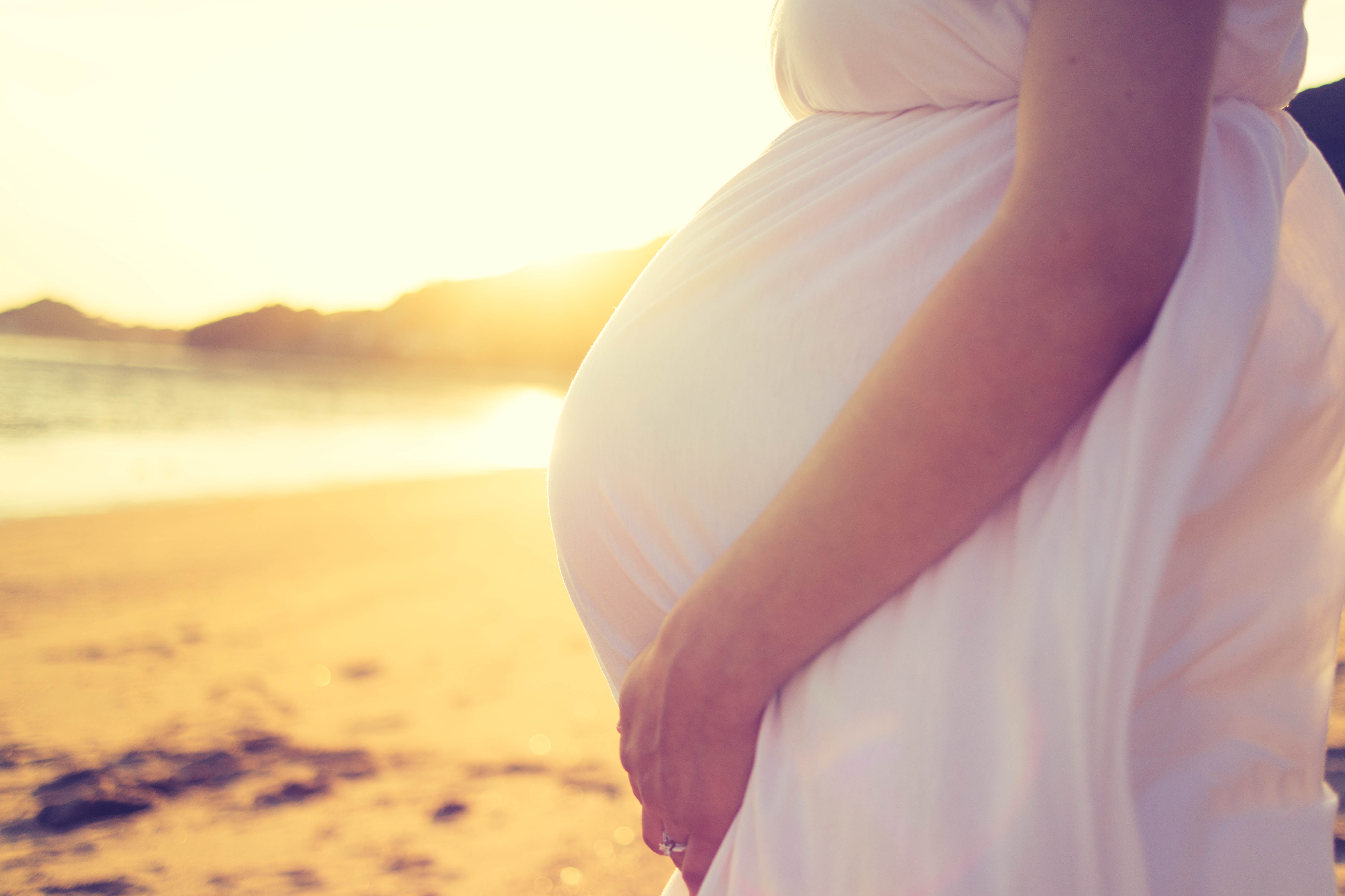 This image shows a pregnant woman on a beach at sunset.