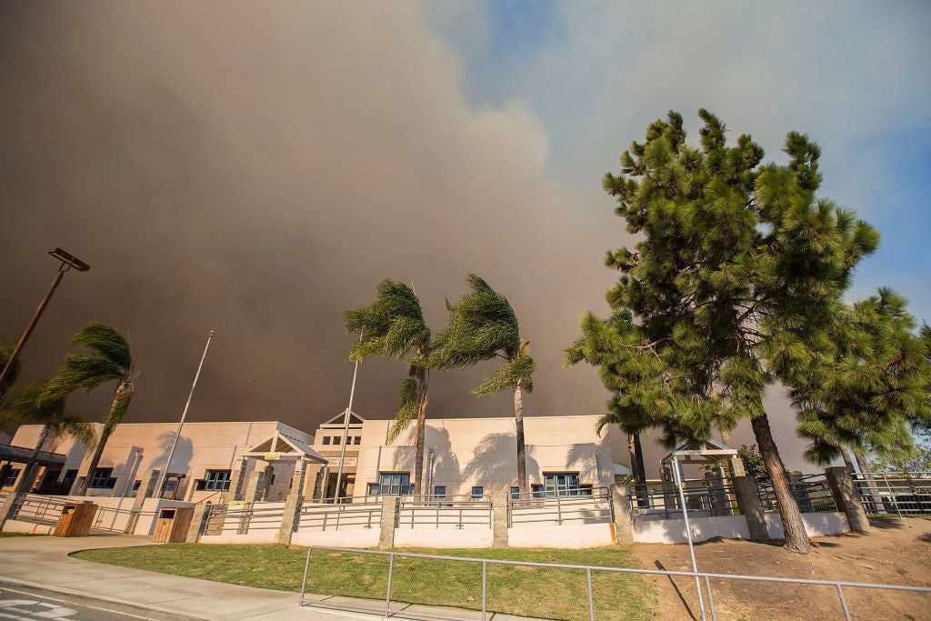A thick cloud of smoke rises behind a middle school near San Diego as the Lilac Fire nears in 2017.
