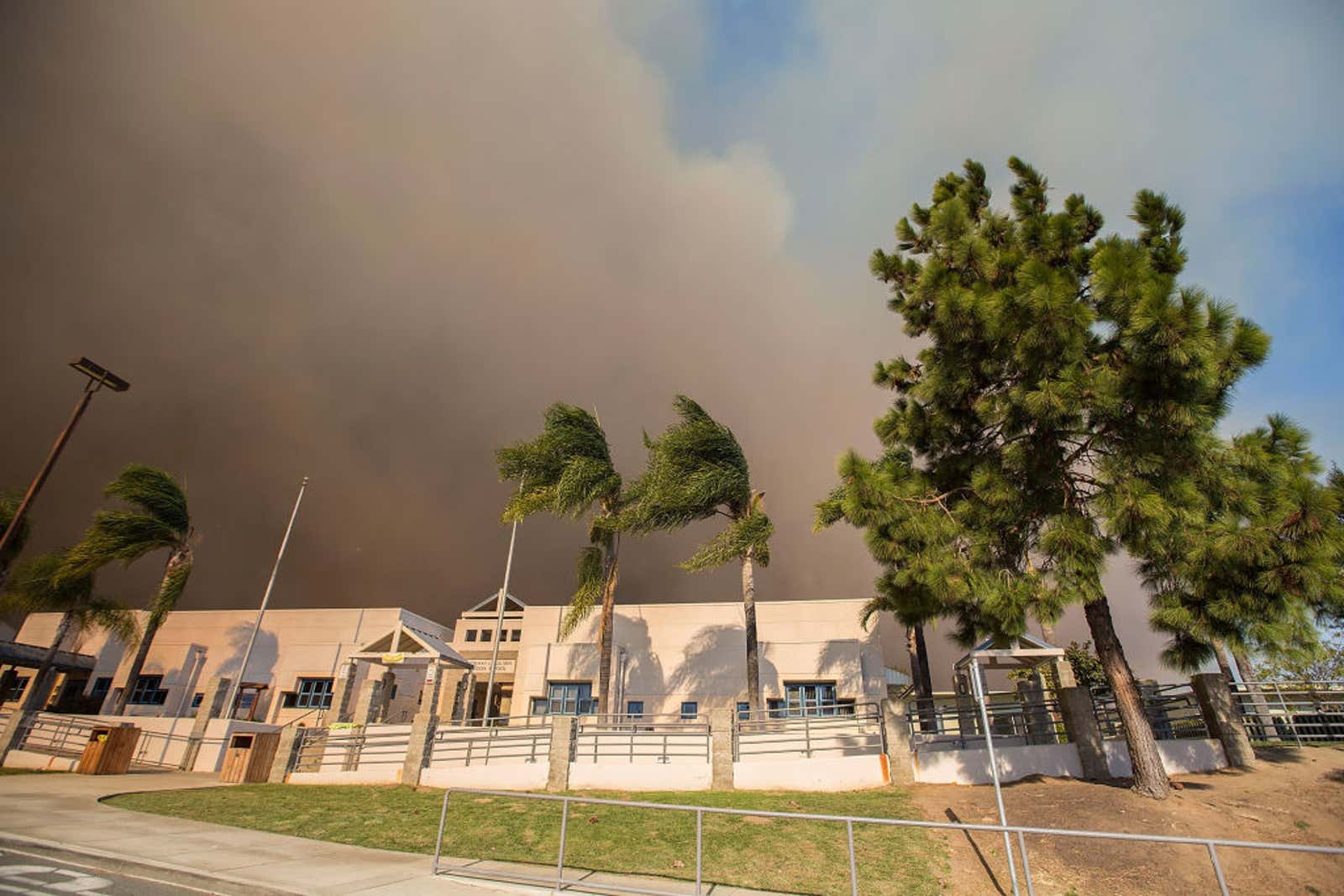 A thick cloud of smoke rises behind a middle school near San Diego as the Lilac Fire nears in 2017.