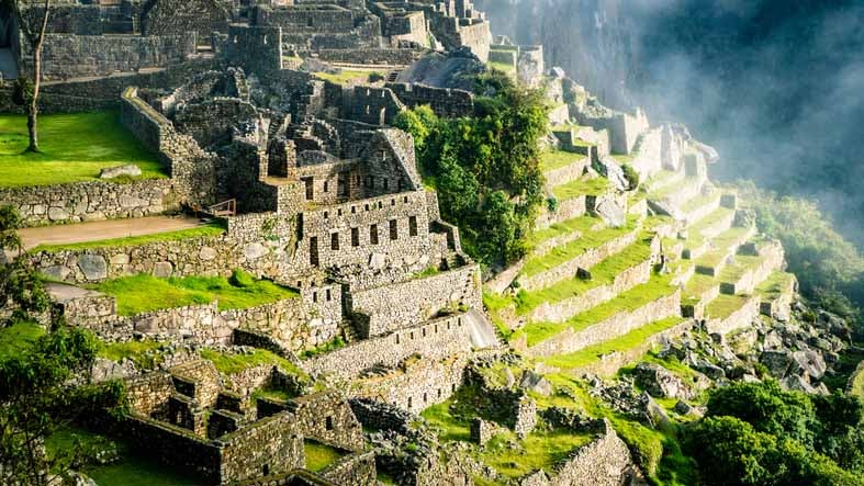 Stone ruins and terraced hillside of Machu Picchu shrouded in mist.