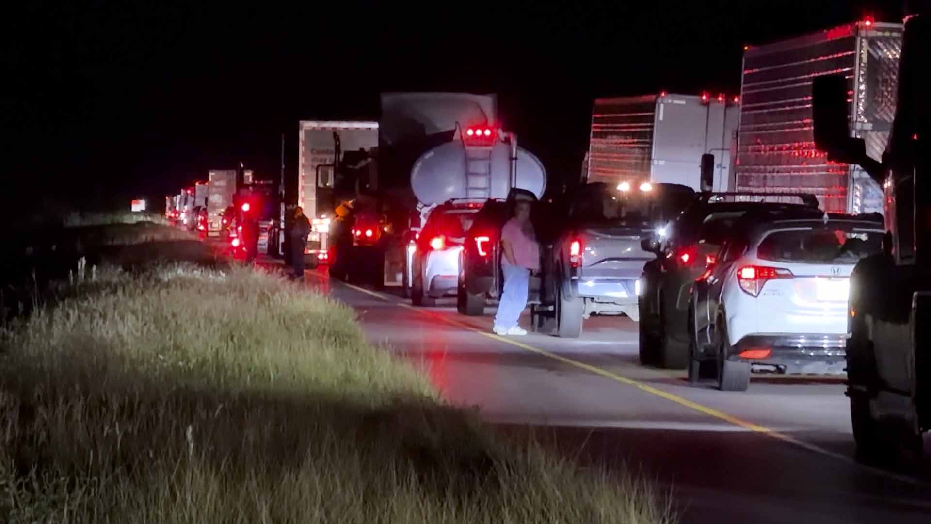 Nighttime highway traffic jam with trucks and cars stopped bumper to bumper, red taillights illuminated.