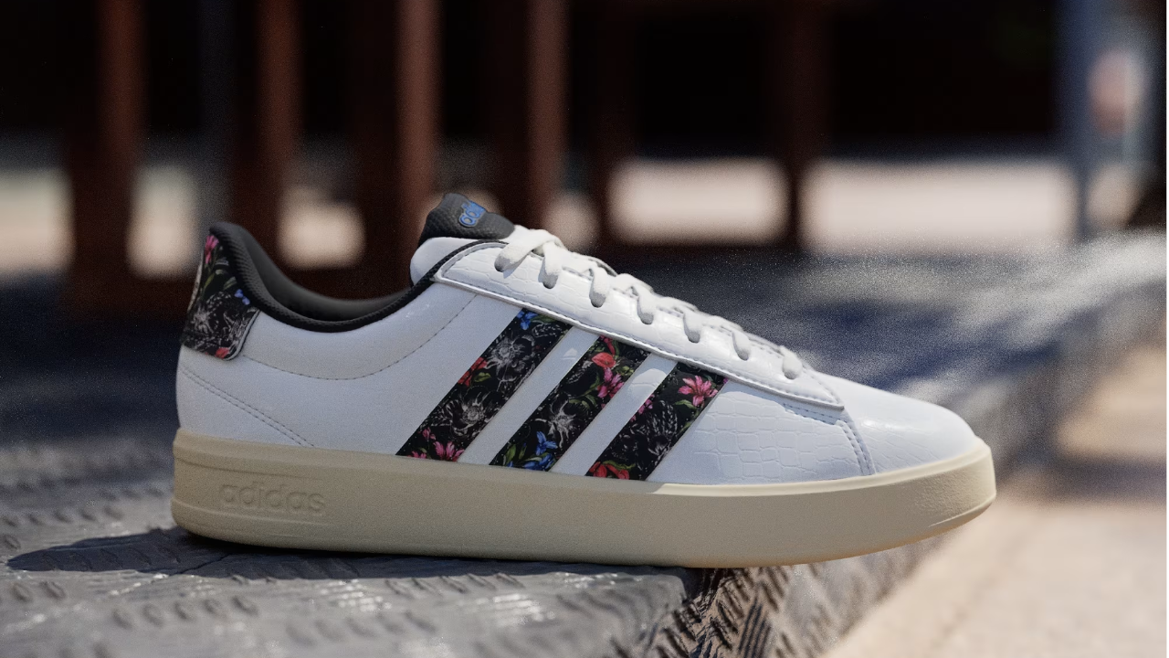 White Adidas sneaker with floral-print stripes and cream sole, displayed outdoors on a textured ledge