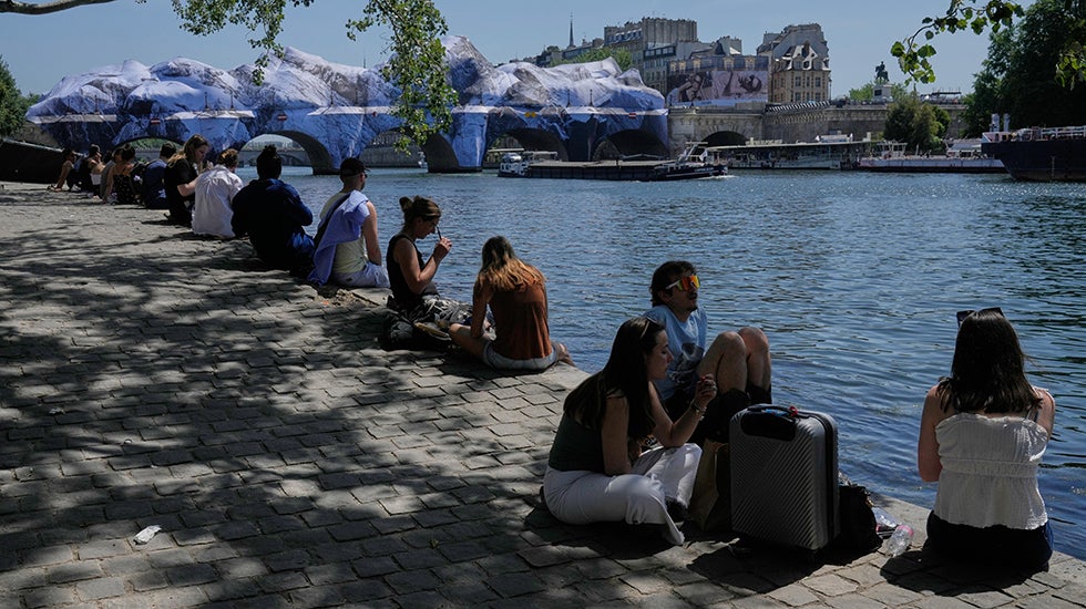 People seek relief from the heat along the Seine River in Paris, Monday, May 25, 2026. Artwork by street artist JR is seen on the Pont Neuf in the background. 