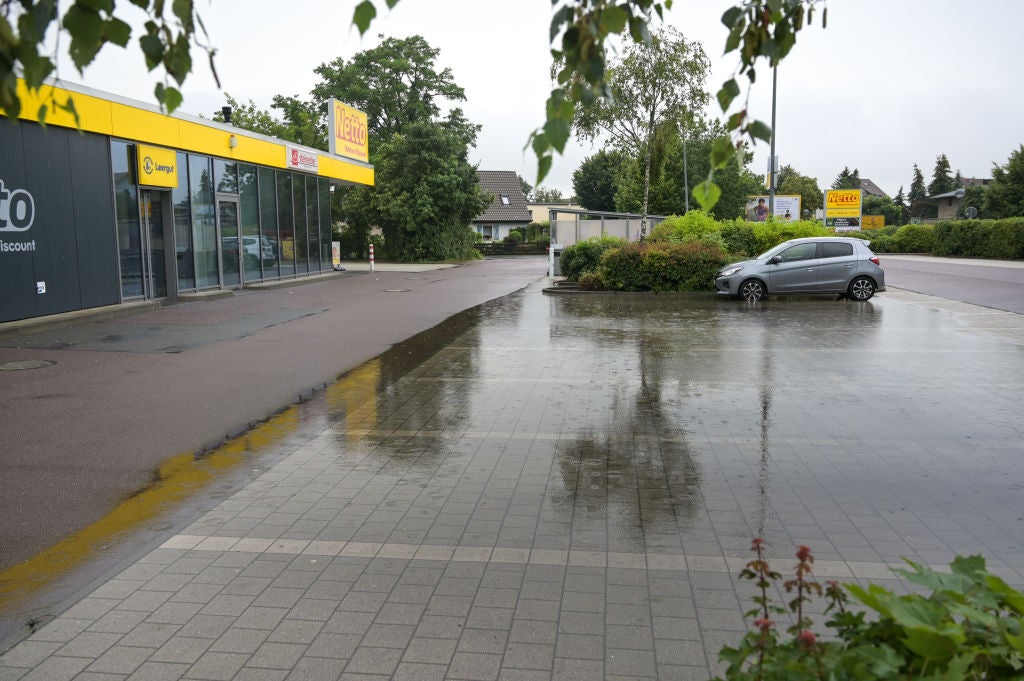 Wet pavement outside a Netto discount store with a gray car parked near green shrubs