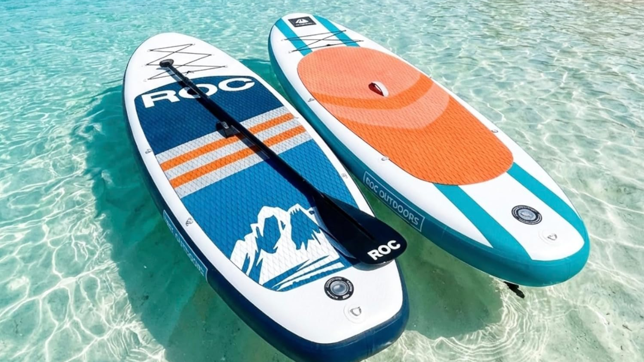 Two inflatable paddle boards floating on crystal clear turquoise water, one with ROC branding and mountain graphics, the other with orange deck pad