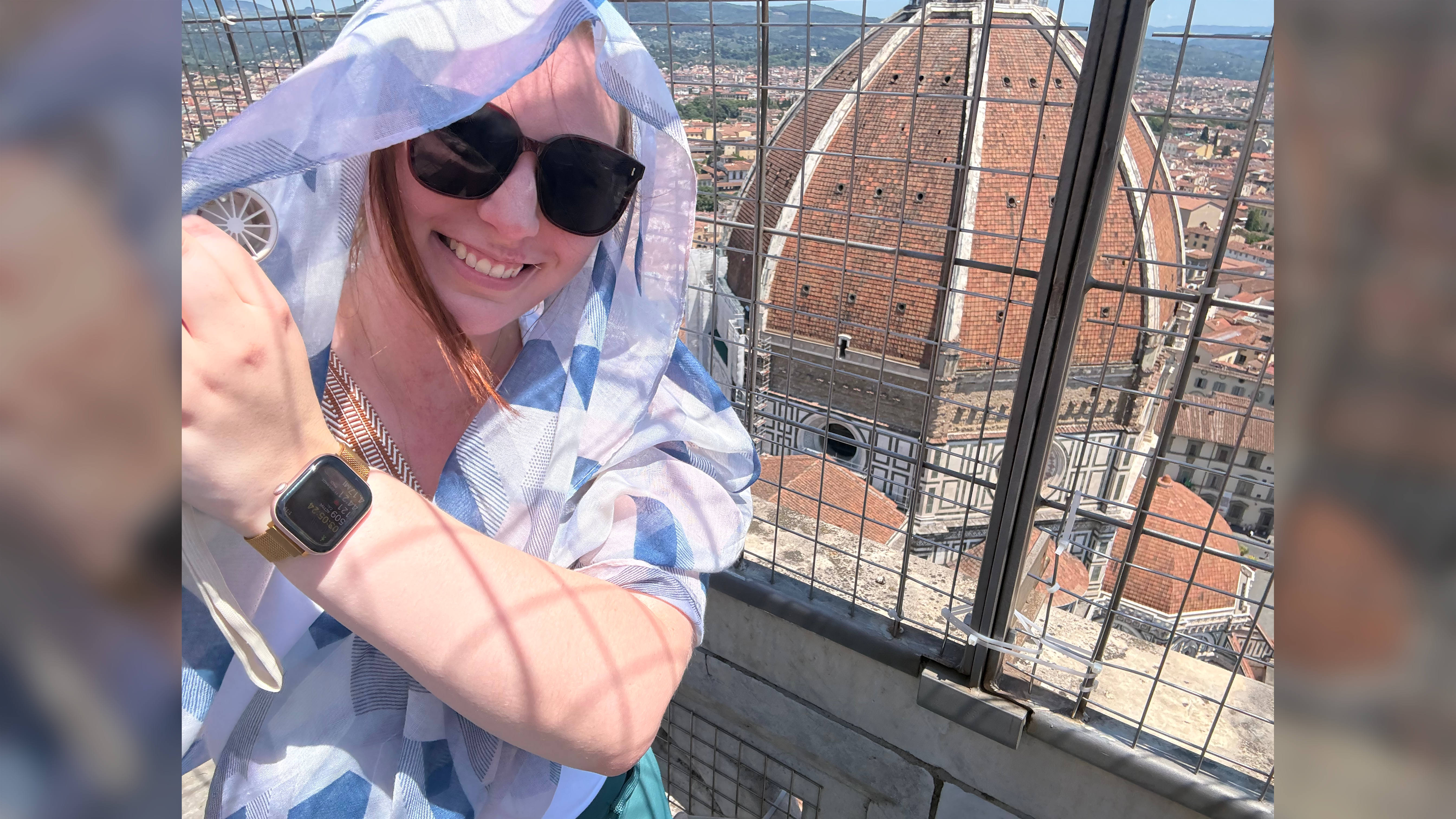 Smiling woman in sunglasses and a headscarf poses on a high lookout with Florence cathedral dome in the background