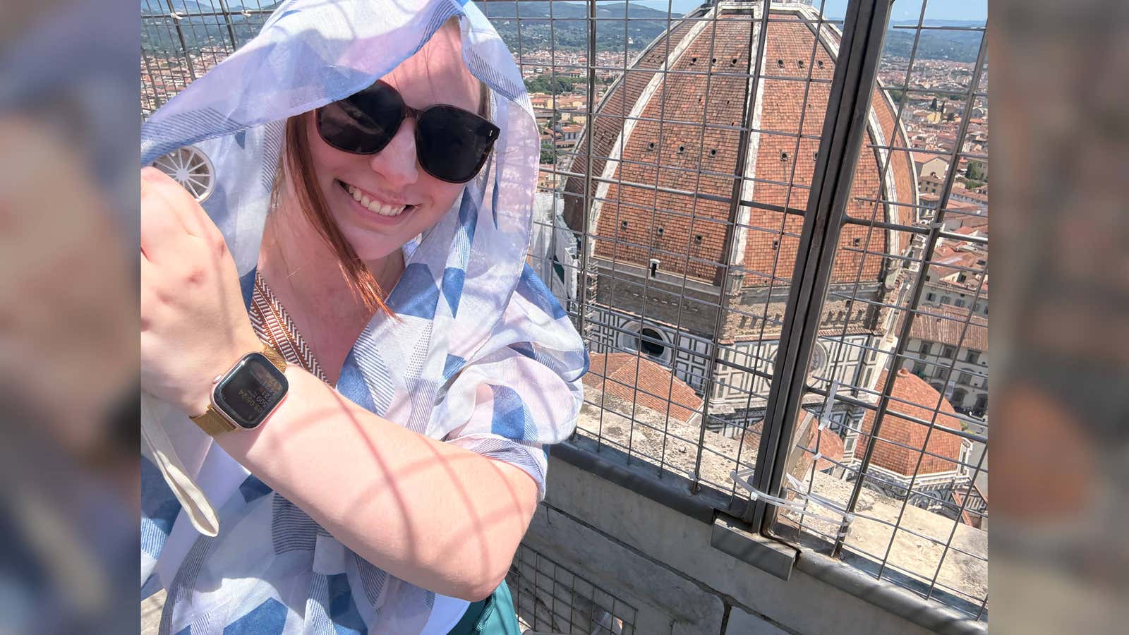 Smiling woman in sunglasses and a headscarf poses on a high lookout with Florence cathedral dome in the background
