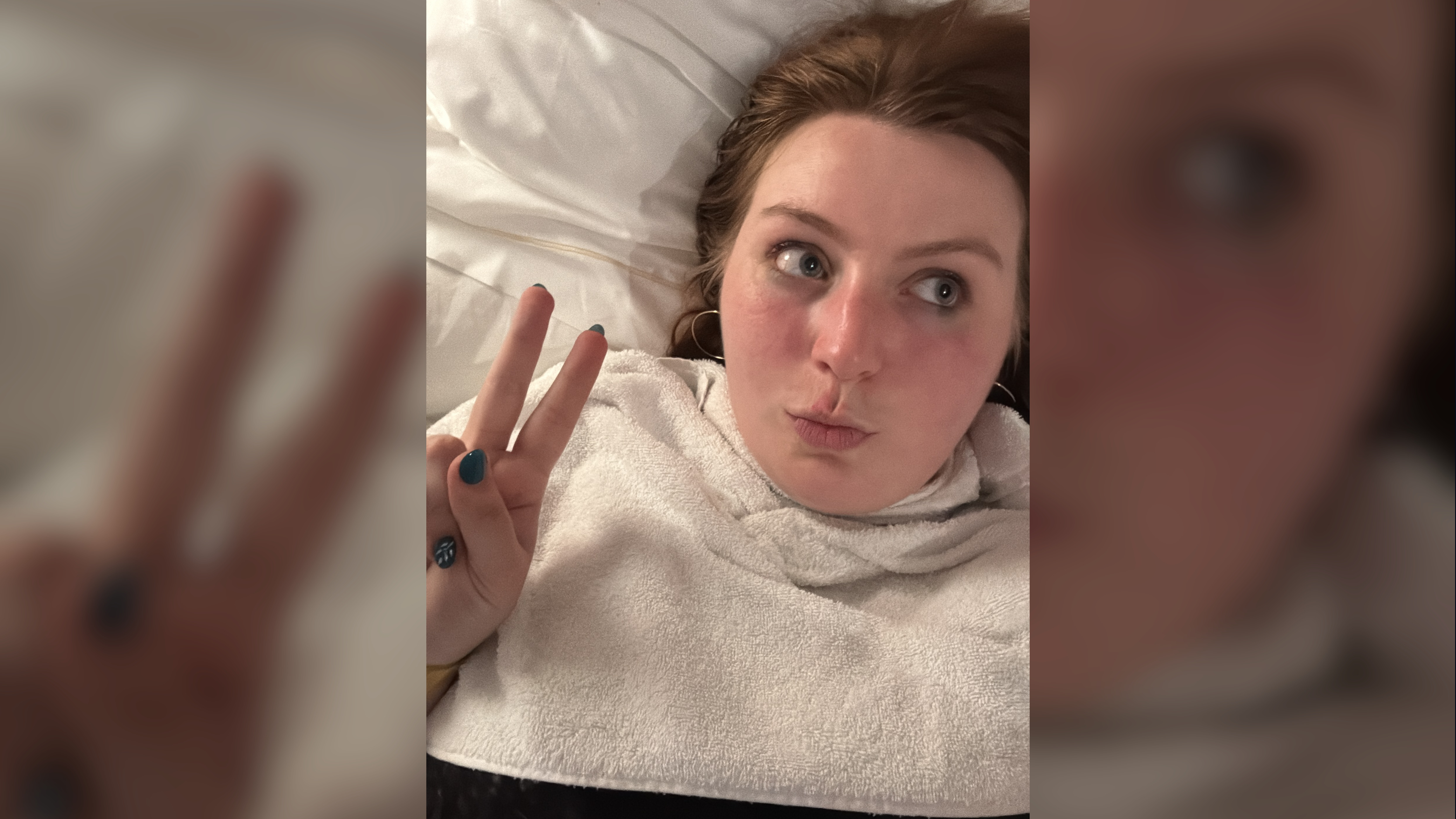 Woman lying on a bed making a peace sign, wearing a white towel and teal nail polish