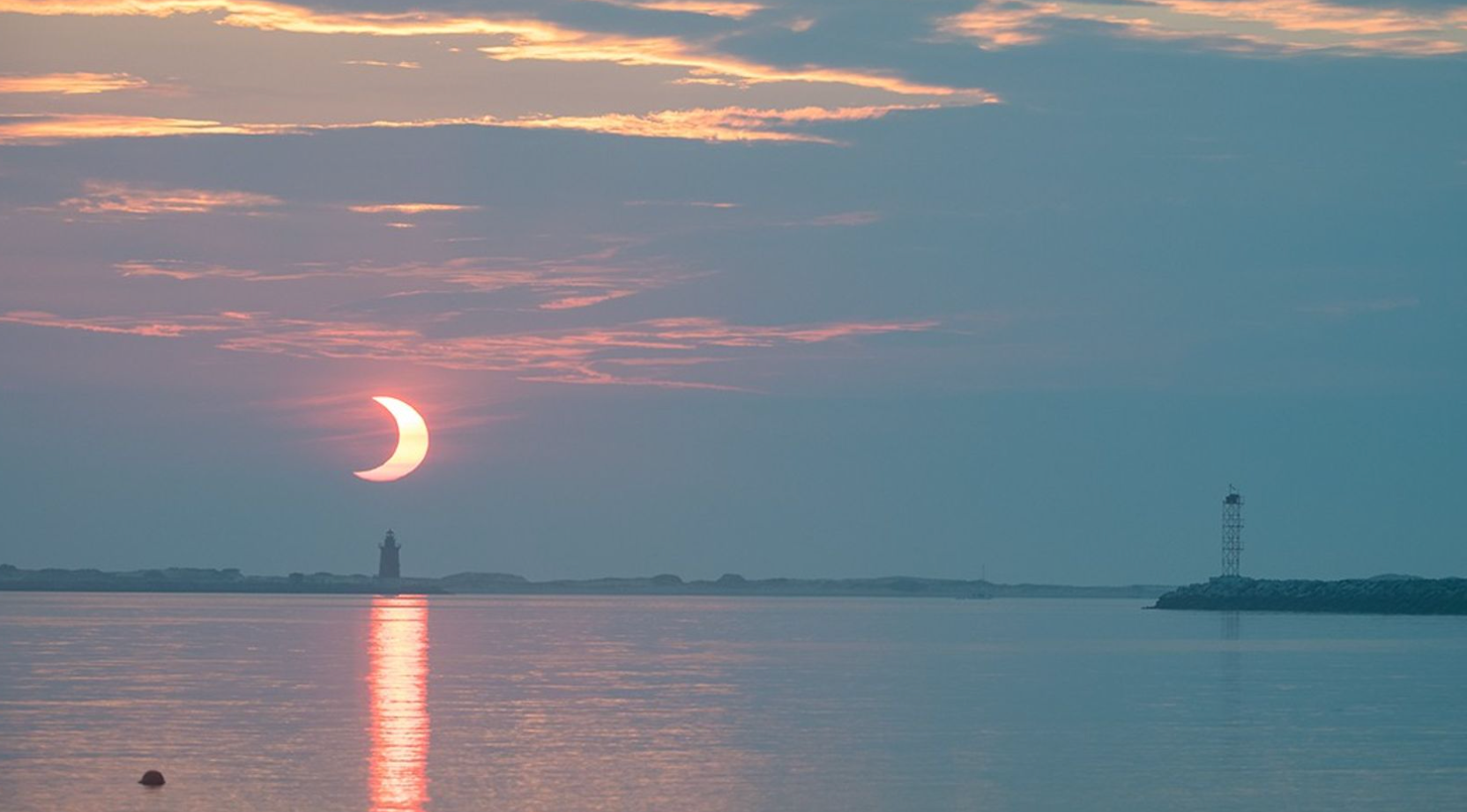 A partial solar eclipse is seen as the Sun rises behind the Delaware Breakwater Lighthouse on June 10, 2021, at Lewes Beach in Delaware.