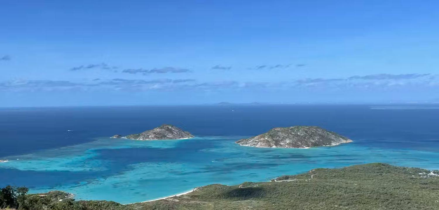 Aerial view of two small rocky islands surrounded by turquoise waters and coral reefs under a blue sky