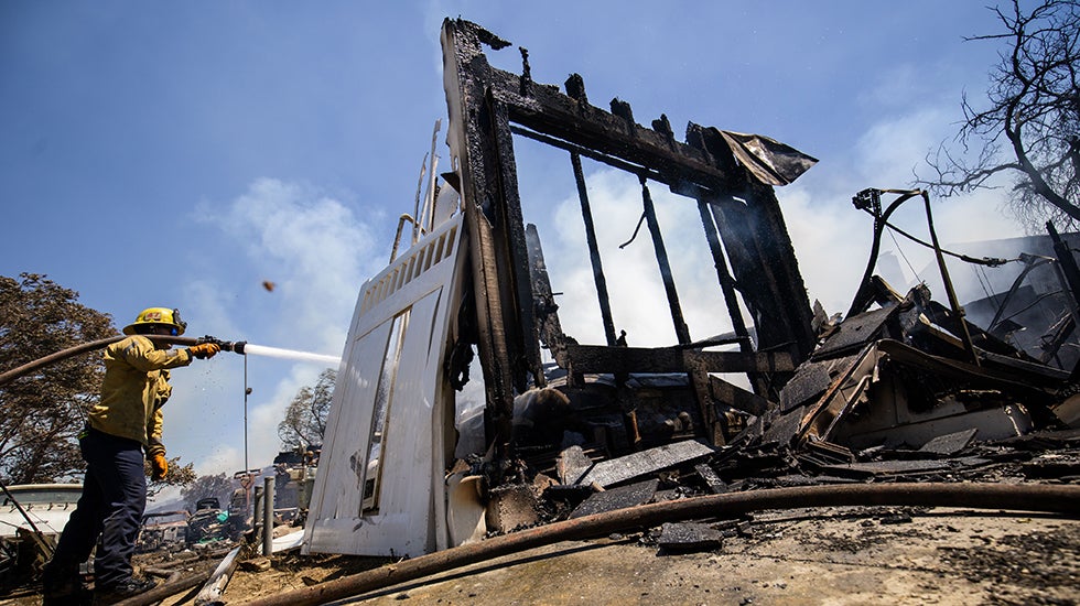 A firefighter hoses down hotspots at a property damaged by the Sandy Fire Monday, May 18, 2026, in Simi Valley, Calif. (AP Photo/Ethan Swope)