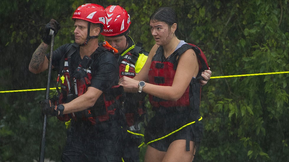 A woman is led along a rope by firefighters